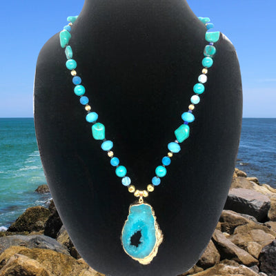 This necklace is crafted with beautiful indigo, turquoise, crystal, and gold plated beads, and features a bold pendant that makes a statement